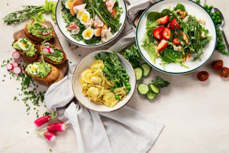 Téléchargez les photos : Nourriture fraîche printanière avec feuille verte. Salades aux fraises, bacon et raviolis sur fond bois clair. Vue du dessus - en image libre de droit