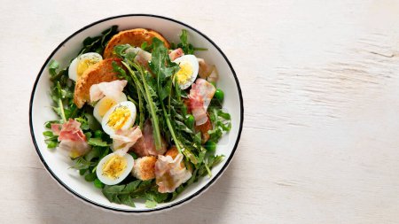 Téléchargez les photos : Salade fraîche estivale à base de feuilles de pissenlit, œufs, bacon et pain sur fond clair. Vue du dessus, espace de copie - en image libre de droit