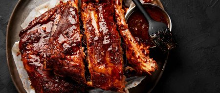 Photo for Hot grilled spare ribs from a summer BBQ served on a plate with sauce. Top view. Panorama with copy space. - Royalty Free Image