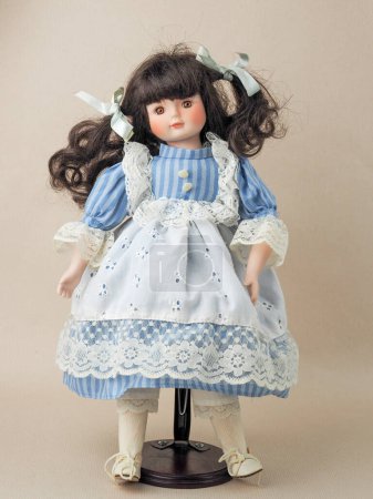 Photo for Vintage porcelain doll girl with brown eyes brunette with braided ribbons in a blue dress with white vertical stripes and a lace apron. - Royalty Free Image