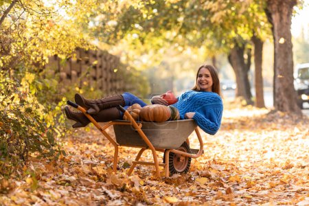 Photo for Woman have fun, lying in the garden wheelbarrow with pumpkins, thanksgiving selebrating - Royalty Free Image