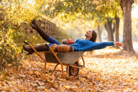 Photo for Woman have fun, lying in the garden wheelbarrow with pumpkins, thanksgiving selebrating - Royalty Free Image