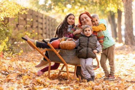 Photo for Mother have fun time with kids, use garden wheelbarrow with pumpkins. Autumn, thankgiving time - Royalty Free Image