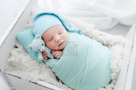 Foto de Newborn baby child swaddled in fabric sleeping and holding teddy bear toy. Sweet infant kid napping on fur in tiny bed - Imagen libre de derechos