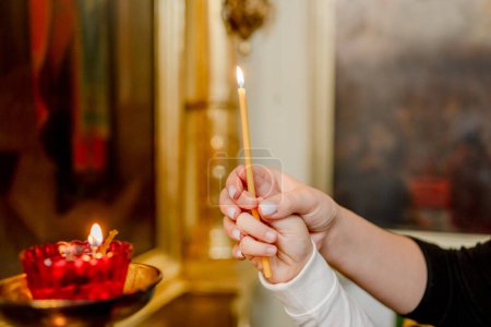 La mano de una mujer y un niño puso una vela en la Iglesia Ortodoxa