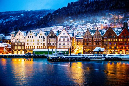 Winter Bergen Stadt mit berühmten Bryggen Merchandise-Holzhäusern und Lichtern in der Schneezeit. Panorama historischer Hafengebäude zur Weihnachtszeit mit magischer Spiegelung im Meer