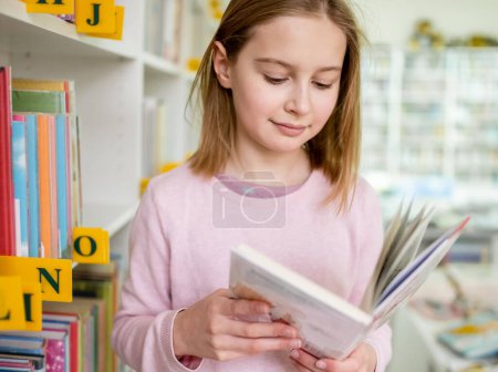 Photo for Pretty girl child reading book in library. Cute female preteen kid studying literature in biblioteque - Royalty Free Image