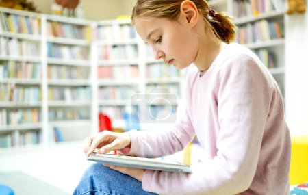 Téléchargez les photos : Jolie fille enfant lecture livre à la bibliothèque. Jeune fille mignonne pré-adolescente étudiant la littérature en biblioteque - en image libre de droit