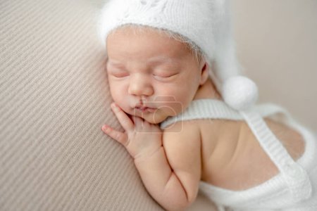 Téléchargez les photos : Un nouveau-né portant un pantalon tricoté et un chapeau dormant sur son ventre. Enfant bébé enfant sieste et tient la main sous la joue - en image libre de droit
