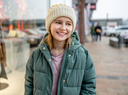 Photo for Preteen girl smiling at street portrait in city with blurred background. Cute female child kid wearing hat outdoors at autumn time - Royalty Free Image