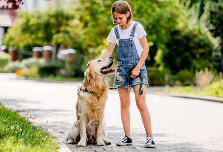 Photo for Preteen girl with golden retriever dog walking at street. Pretty child kid with purebred dog labrador in park outdoors. - Royalty Free Image