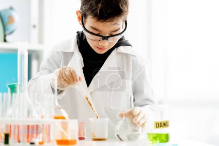 Photo for School boy wearing protection glasses with dirty face doing chemistry experiment with chemical liquids in elementary science class. Clever pupil analyzing results of test in lab - Royalty Free Image