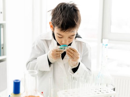 Foto de Niño de escuela con lente de zoom durante el experimento químico en la clase de ciencias elementales. Un alumno inteligente en el laboratorio - Imagen libre de derechos