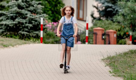 Téléchargez les photos : Little girl riding a kick scooter on a street near home - en image libre de droit
