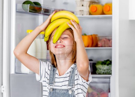 Foto de Preteen girl with bananas vitamin healthy food at kitchen. Pretty child kid enjoying yellow fruits at home - Imagen libre de derechos