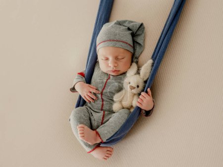 Téléchargez les photos : Bébé garçon nouveau-né dormant avec un jouet tricoté pendant la séance photo en studio. Adorable enfant en bas âge enfant dormant portant chapeau et costume - en image libre de droit