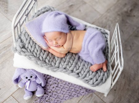 Photo for Newborn baby boy sleeping on tiny bed with bunny toy. Little infant child napping wearing knitted pants and hat - Royalty Free Image