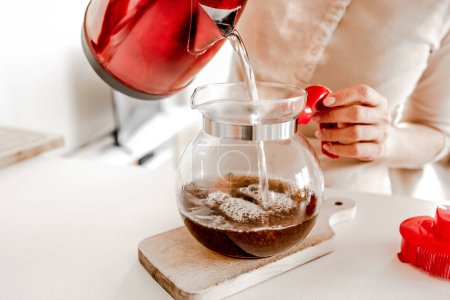 Téléchargez les photos : Girl pouring with hot tea from teapot cups at kitchen. Woman preparing warm herbal beverage with kettle and mugs - en image libre de droit