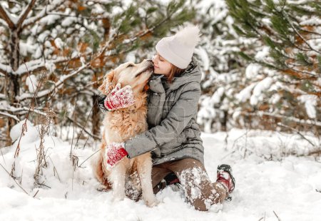 Téléchargez les photos : Girl petting and hugging golden retriever dog sitting in snow in winter time. Young woman with doggy pet outdoors in cold weather with snowflakes - en image libre de droit