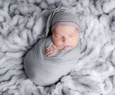 Photo for Cute newborn baby boy swaddled in grey fabric sleeping on fur blanket. Adorable infant child kid napping studio portrait - Royalty Free Image