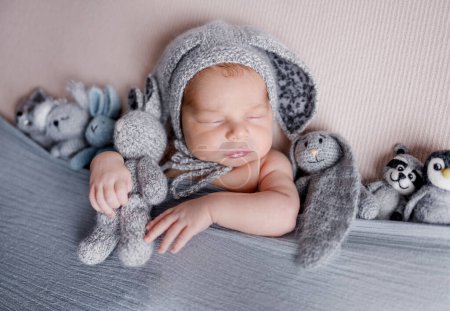 Photo for Cute newborn baby boy sleeping wearing bunny ears hat and holding knitted handmade toys. Adorable infant child kid napping studio portrait - Royalty Free Image