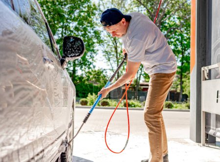 Téléchargez les photos : Un homme lave une voiture à un lave-auto libre-service avec une brosse - en image libre de droit