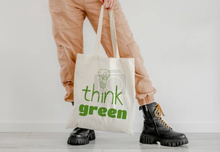 Foto de Girl holding cotton linen eco bag with text think green. Woman with environment friendly reusing shopping handbag - Imagen libre de derechos