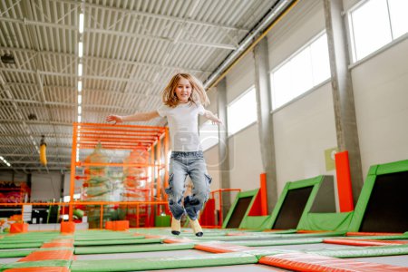 Foto de Pretty girl in trampoline park jumping with split and smiling. Happy little enjoying amusement activities - Imagen libre de derechos