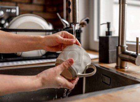 Foto de Girl filling cup with kitchen tap water at home. Woman pouring mug with transparent pure beverage flow - Imagen libre de derechos