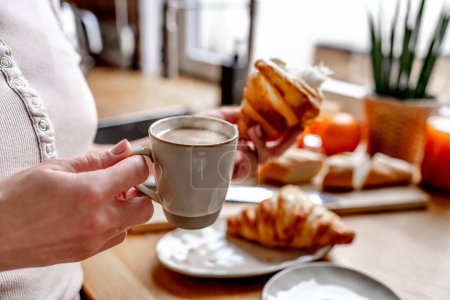 Photo for Girl holding cappuccino coffee mug and croissant at kitchen for french breakfast. Woman with pastry and espresso - Royalty Free Image