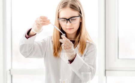 Photo for Smart girl during scientific chemistry experiment wearing protection glasses, holding tubes and measuring ingridients. Schoolgirl with chemical equipment on school lesson - Royalty Free Image