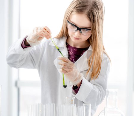 Foto de Chica inteligente durante el experimento de química científica con gafas de protección, la celebración de tubos y la medición de ingridientes. Colegiala con equipo químico en la lección escolar - Imagen libre de derechos