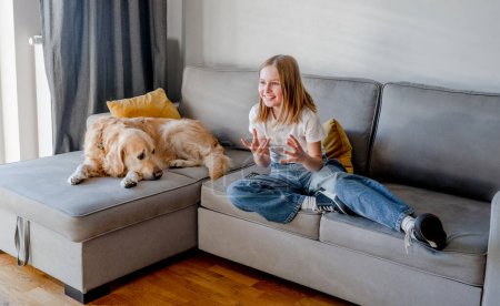 Photo for Preteen girl with golden retriever dog watching tv with emotions at home. Beautiful child kid with labrador doggy pet looking cartoons at television sitting on sofa - Royalty Free Image
