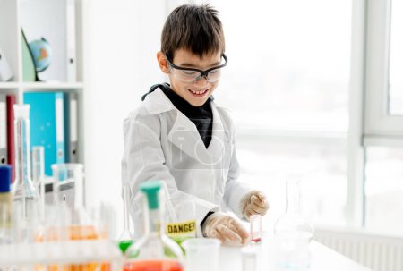 Téléchargez les photos : Un écolier portant des lunettes de protection faisant des expériences de chimie en classe de sciences élémentaires. Elève avec tubes d'équipement en laboratoire - en image libre de droit