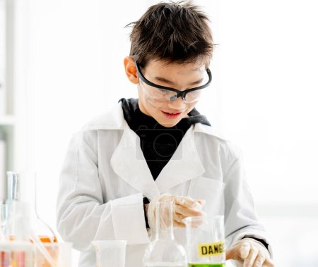 Foto de Niño de la escuela con gafas de protección con la cara sucia haciendo experimento químico con líquidos químicos en la clase de ciencias elementales. Alumno inteligente analizando los resultados de la prueba en el laboratorio - Imagen libre de derechos