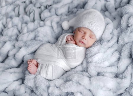 Foto de Lindo bebé recién nacido envuelto en tela gris durmiendo en manta de piel. Adorable bebé niño siesta estudio retrato - Imagen libre de derechos