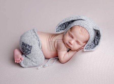 Foto de Lindo niño recién nacido durmiendo con sombrero de orejas de conejo y pantalones de punto. Adorable bebé niño siesta estudio retrato - Imagen libre de derechos