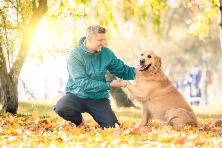 Foto de Hombre jugando con su perro golden retriever en el parque de otoño - Imagen libre de derechos