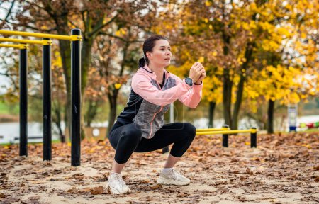 Foto per Fitness ragazza che fa squat outdoots in autunno. Giovane donna che si esercita nel parco nella stagione autunnale - Immagine Royalty Free