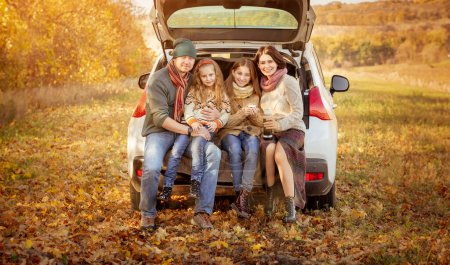 Photo for Happy family sitting in car trunk on autumn background - Royalty Free Image