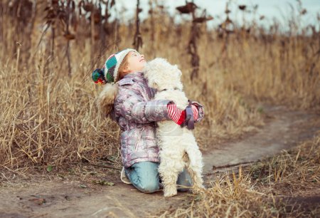 Foto de Pequeña linda chica con su perro crianza blanco terrier caminar en un campo - Imagen libre de derechos