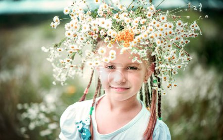 Foto de Niña de seis años con una corona en la cabeza en el campo con manzanillas - Imagen libre de derechos