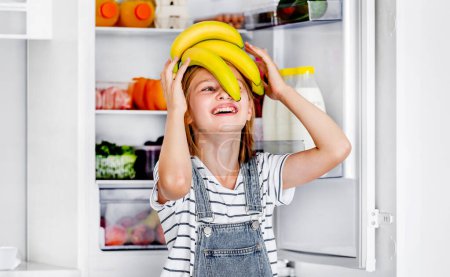 Téléchargez les photos : Preteen girl with bananas vitamin healthy food at kitchen. Pretty child kid enjoying yellow fruits at home - en image libre de droit