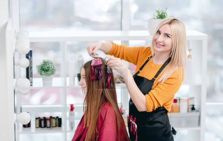Photo for Hairdresser shows colorful samples for hair dyeing to beautiful model girl client and smiling - Royalty Free Image