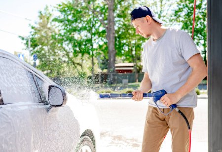 Téléchargez les photos : Un homme lave une voiture dans un lave-auto libre-service avec de la mousse - en image libre de droit