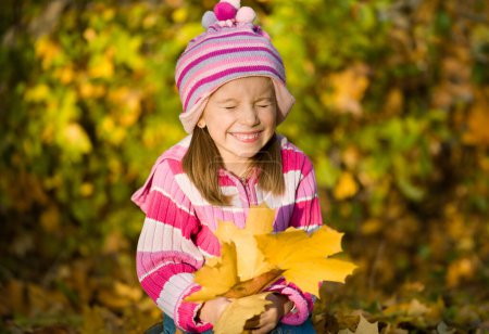 Photo for Little girl squinting against autumn leaves - Royalty Free Image