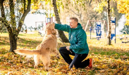 Foto de Hombre jugando con su perro golden retriever en el parque de otoño - Imagen libre de derechos