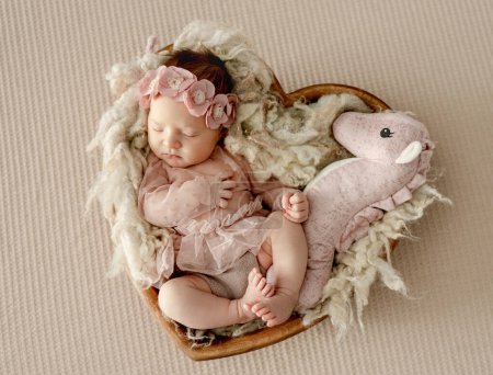 Photo for Newborn baby girl wearing dress sleeping in heart shape basket with toy. Cute infant child kid in wreath napping on fur - Royalty Free Image