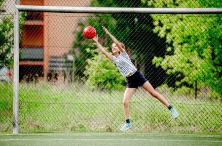 Photo for Pretty child girl catching football ball defending goal. Cute female kid at socker field playing - Royalty Free Image