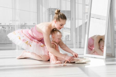 Photo for Two ballerinas, mother and daughter sitting on the twine in front of large windows in studio. Little ballerina girl and her teacher doing the split. Little girl stretching with her mother - Royalty Free Image